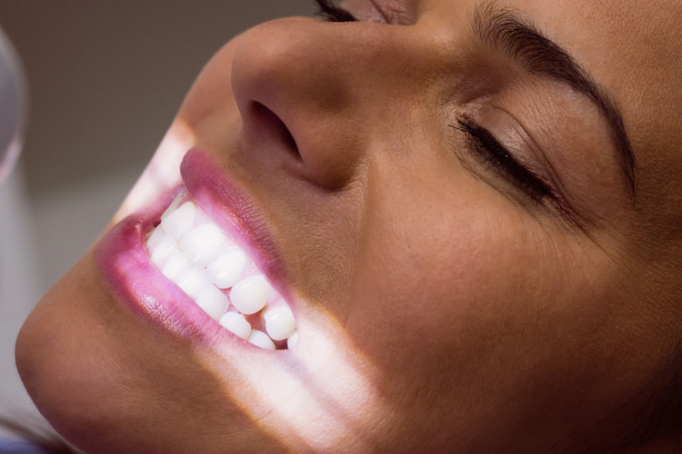 a woman receiving teeth whitening service with light at a dental office.