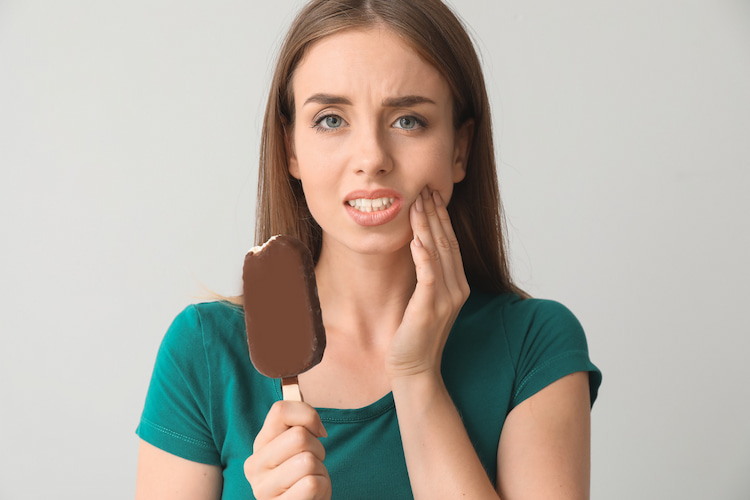 a woman irritated by her sensitive teeth after whitening when eating an ice cream.